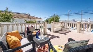 A rooftop terrace with wicker furniture, a table with drinks and a book, and a view of the cityscape. - Villa Karenessa by Villa Plus (Cala en Porter)