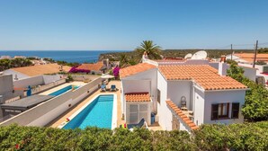 Ein Wohngebiet mit Pool, weißen Gebäuden und roten Ziegeldächern sowie freiem Blick auf das Meer.