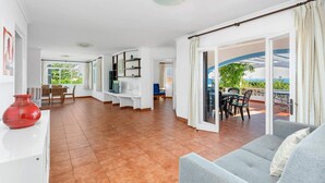 Een ruime woonkamer met een bank, een eettafel en een televisie. Er is een balkon met terrasmeubels.