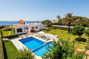 A modern villa with a swimming pool, a view of the sea, and a well-maintained garden.