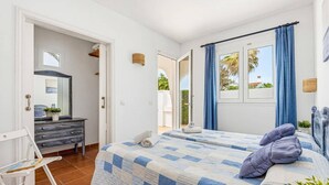 A bedroom with a bed, a dresser, a chair, and a window with curtains. - Villa Ondinas by Villa Plus (Ciutadella de Menorca)