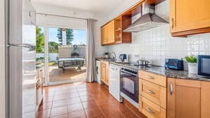 A kitchen with wooden cabinets, a stove, a sink, and a view of a patio with a barbecue grill. - Villa Ondinas by Villa Plus (Ciutadella de Menorca)