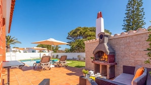 An outdoor patio with a stone oven, lounge chairs, and a pool. - Villa Ondinas by Villa Plus (Ciutadella de Menorca)