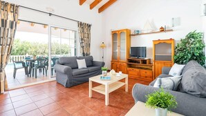 Un amplio salón con un sofá gris, un mueble de madera y una televisión.