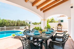 A poolside patio with a table set for dining, a barbecue grill, and a swimming pool.