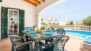 Una terraza con mesa y sillas para dos, piscina y vista a edificios blancos.