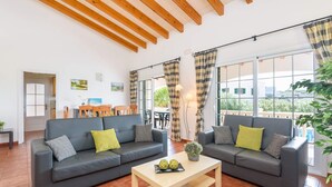 Ett modernt vardagsrum med två grå soffor, ett soffbord i trä och stora fönster med gardiner.