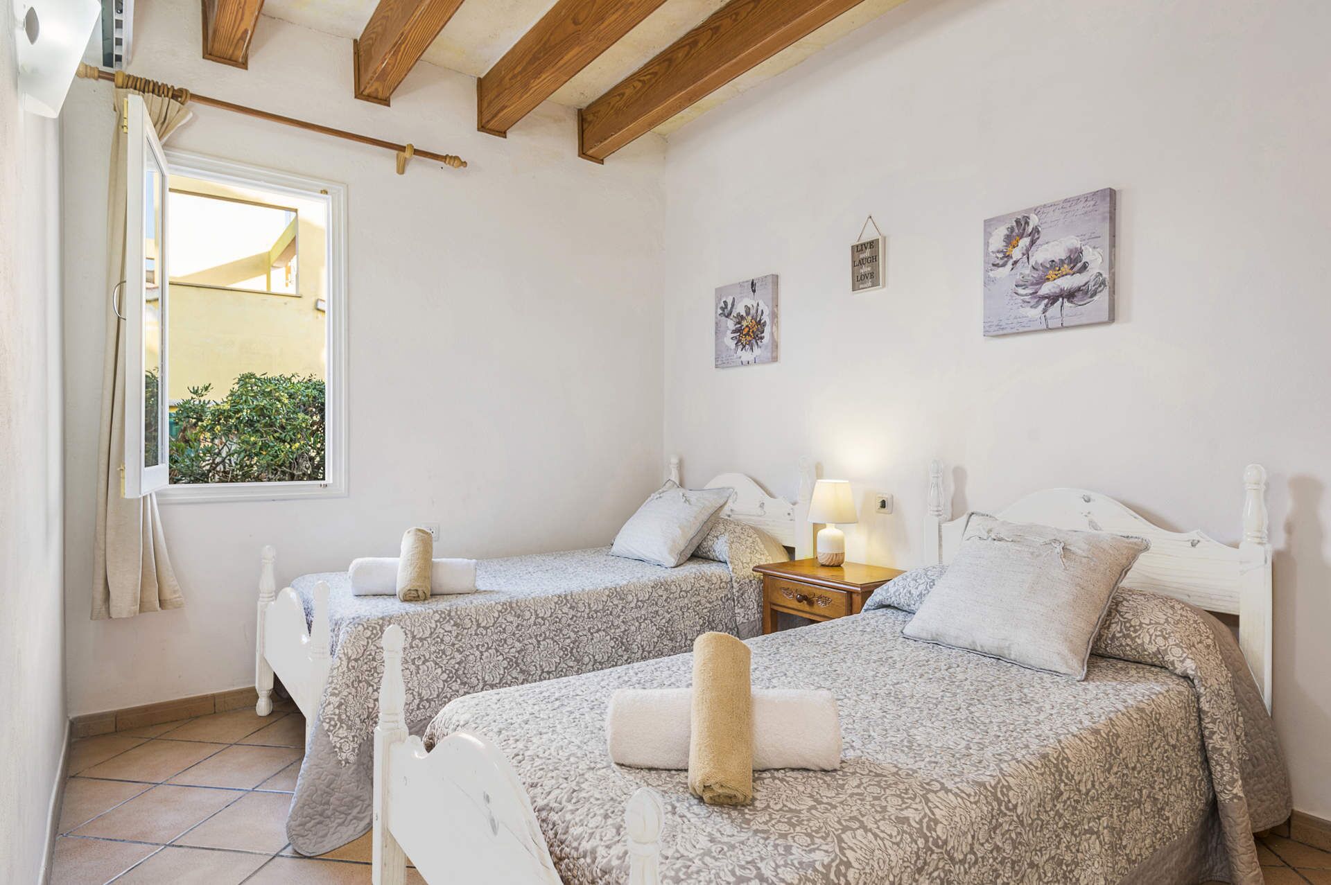A bedroom with two beds, a window with curtains, and a view of greenery outside.