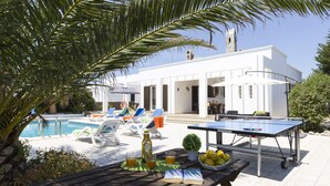 A poolside area with lounge chairs, a ping pong table, and a dining table with drinks and a book. - Villa Solana by Villa Plus (Ciutadella de Menorca)