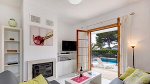 A modern living room with a fireplace, a television, and a pool view. - Villa Solana by Villa Plus (Ciutadella de Menorca)