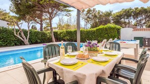 An outdoor dining area with a pool, covered by a canopy, and surrounded by greenery. - Villa Isi by Villa Plus (Ciutadella de Menorca)