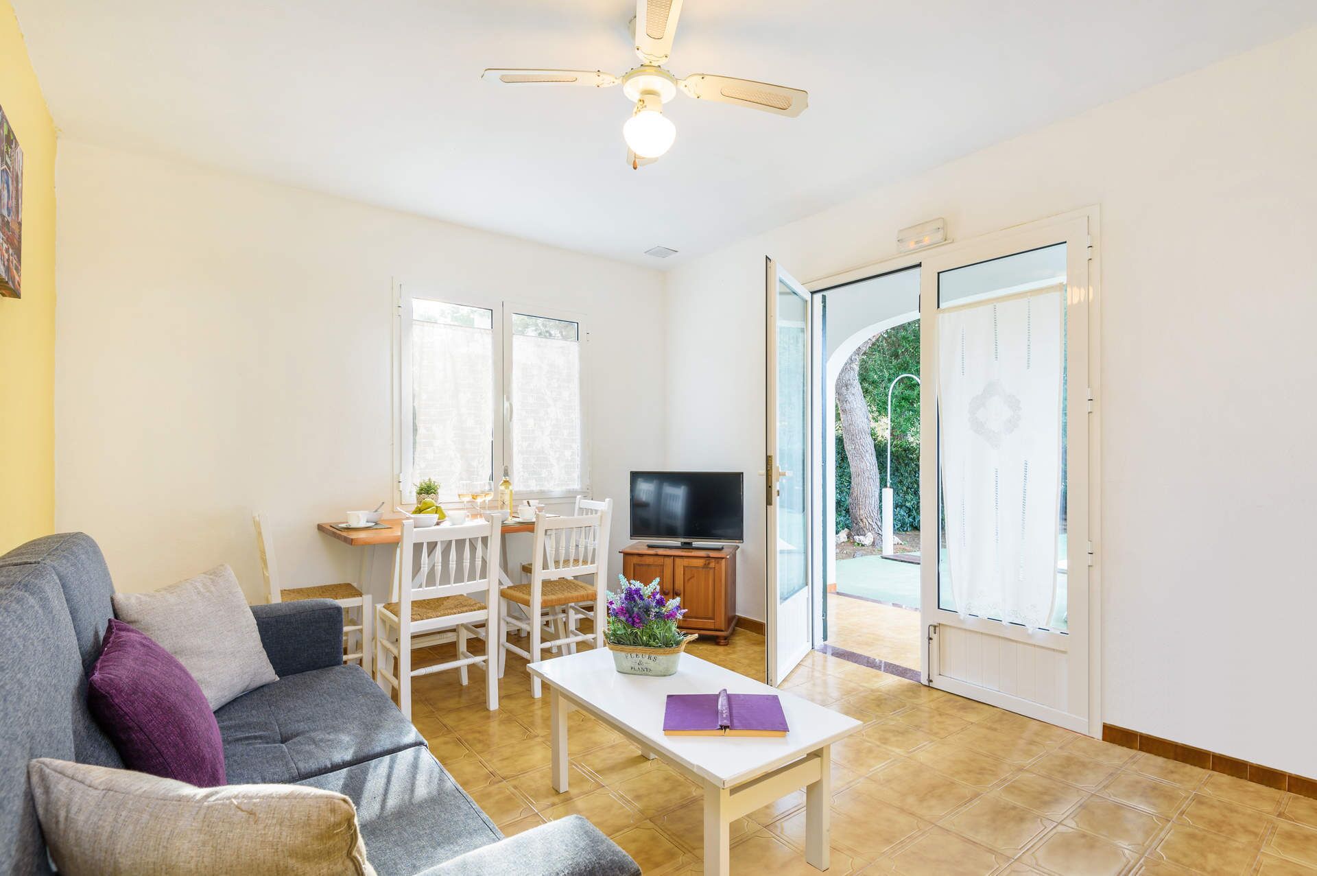 A living room with a sofa, a coffee table, a TV, and a dining area with chairs and a table.