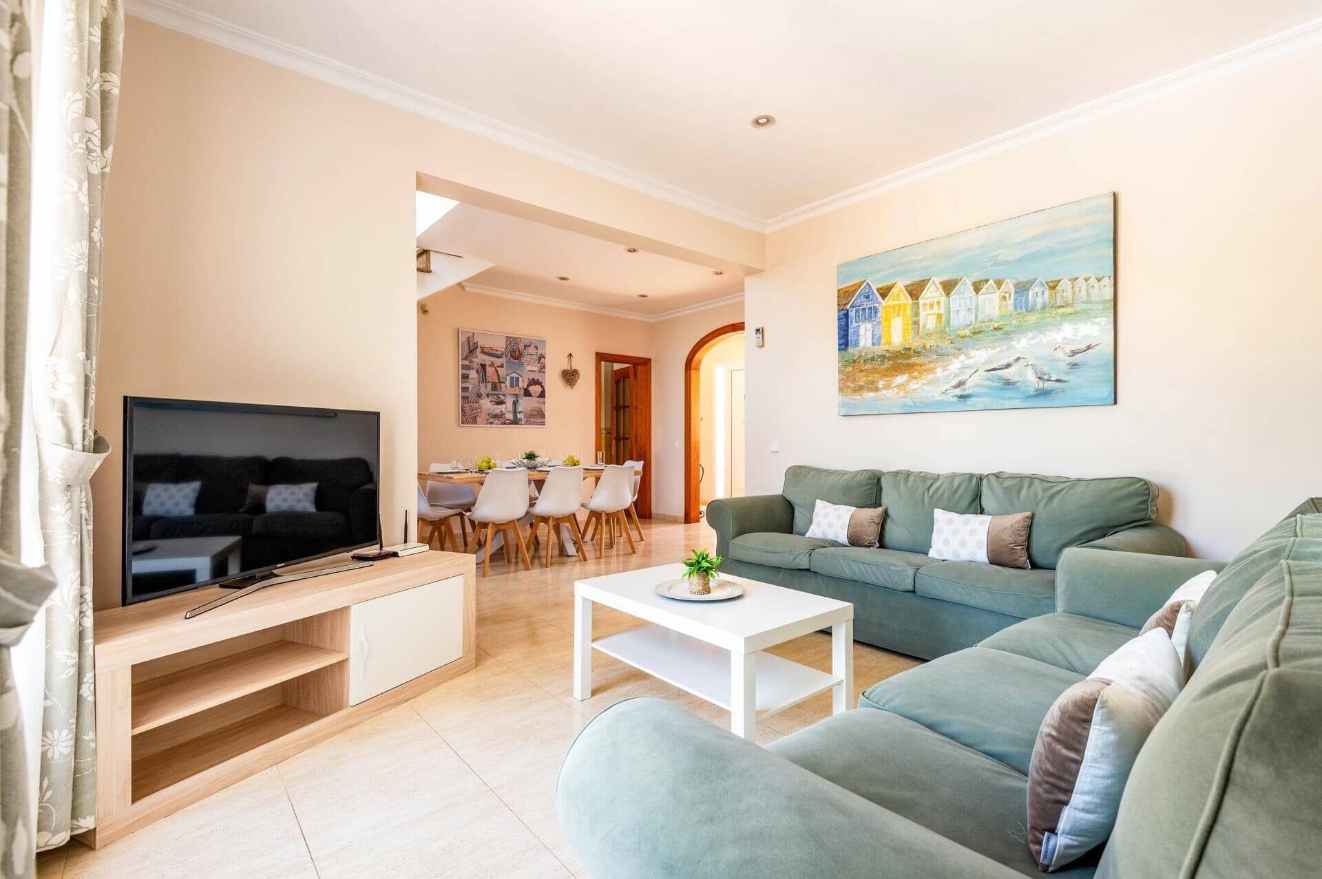 Un salon avec un téléviseur, un canapé, une table basse et un tableau accroché au mur.