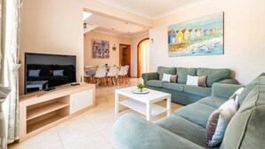 Un salon avec un téléviseur, un canapé, une table basse et un tableau accroché au mur.