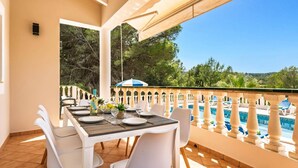 Un espace de restauration en plein air avec une table dressée pour quatre personnes, offrant une vue sur une piscine et une végétation luxuriante.