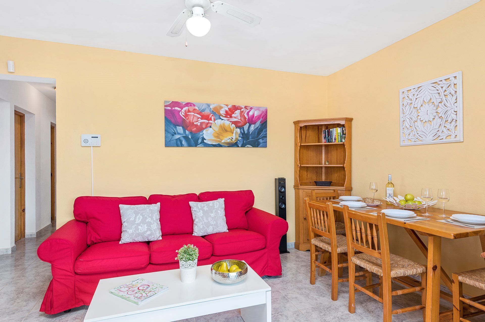 A living room with a red sofa, a white coffee table, and a dining area with a wooden table and chairs.