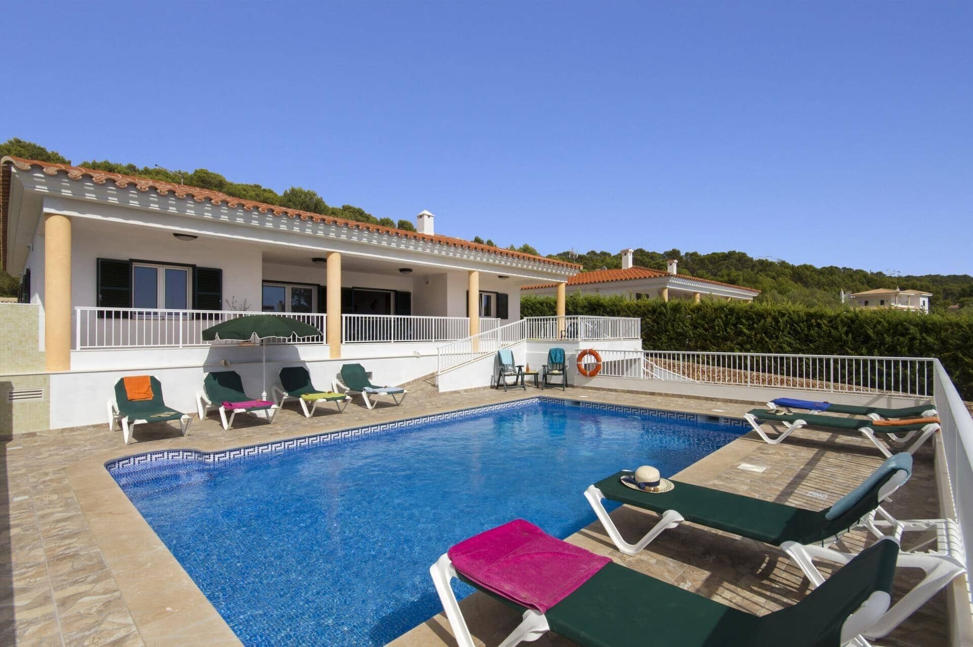 Une piscine avec des chaises longues, une bouée de sauvetage et un bâtiment doté d’un toit en tuiles.