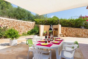 Un espace extérieur aménagé pour les repas, avec un mur en pierre, un four à pizza et une table dressée pour quatre personnes.