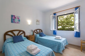 Une chambre avec deux lits, une table de chevet, une fenêtre avec des rideaux et des œuvres d’art mural.