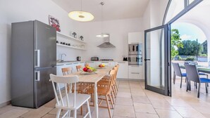 Una cocina moderna con una isla grande, muebles blancos y un comedor con sillas y una mesa.
