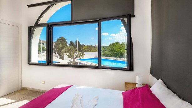 Un dormitorio con un ventanal grande con vistas a una piscina y follaje.
