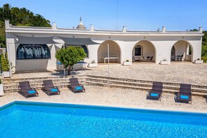 A poolside area with lounge chairs, a swimming pool, and a building with arched windows and a tiled roof.
