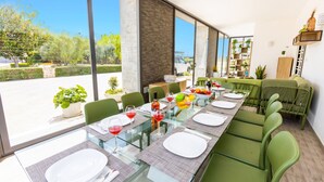 Un coin repas avec une longue table dressée pour six personnes, entourée de chaises vertes, et offrant une vue sur l’extérieur.