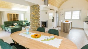 Un vaste espace de vie agrémenté d’une cheminée, d’une table à manger dressée et d’un canapé vert.