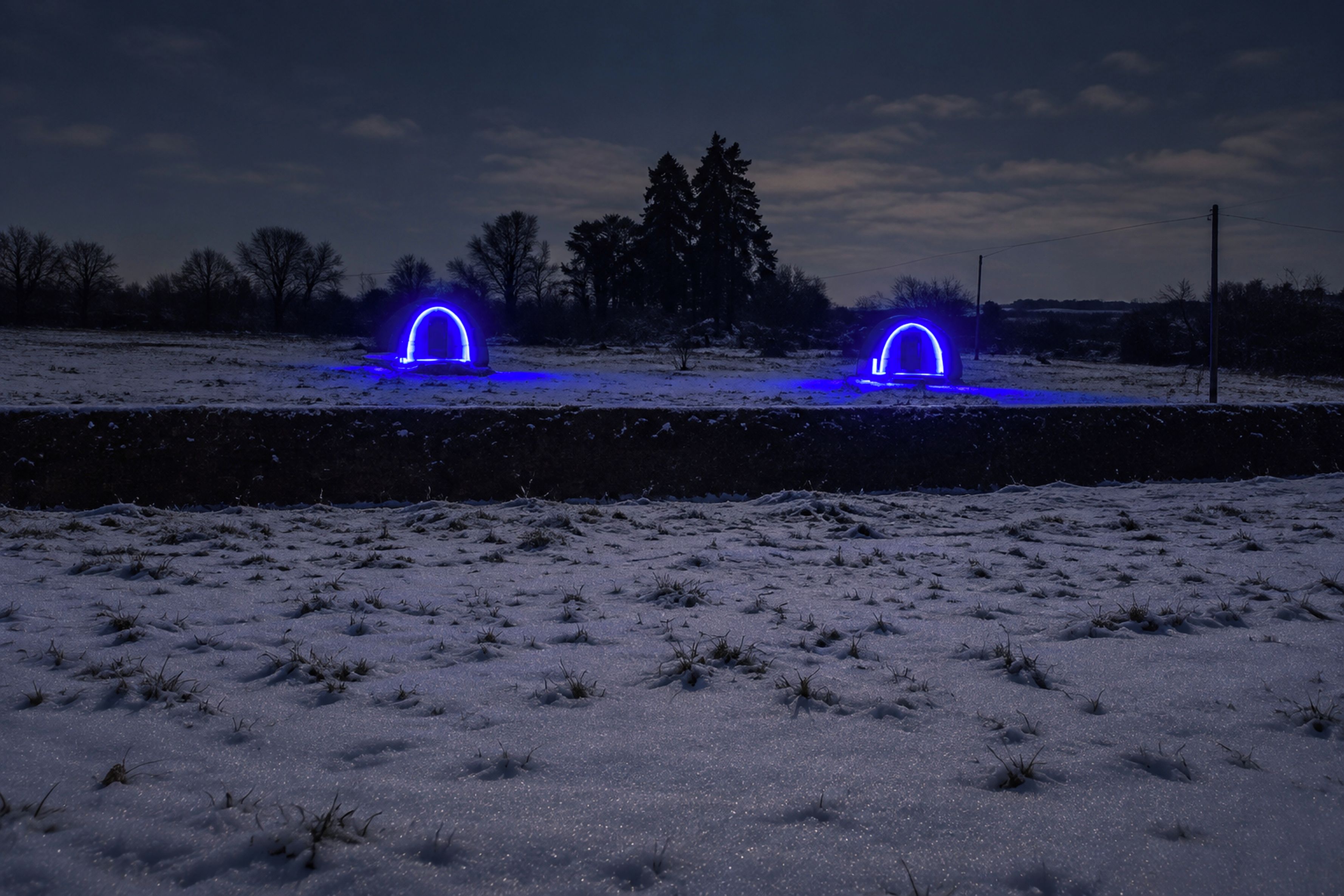A snowy landscape with two illuminated structures resembling arches.