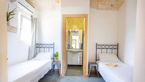 Una habitación pequeña y luminosa con dos camas individuales, una mesita y un espejo.