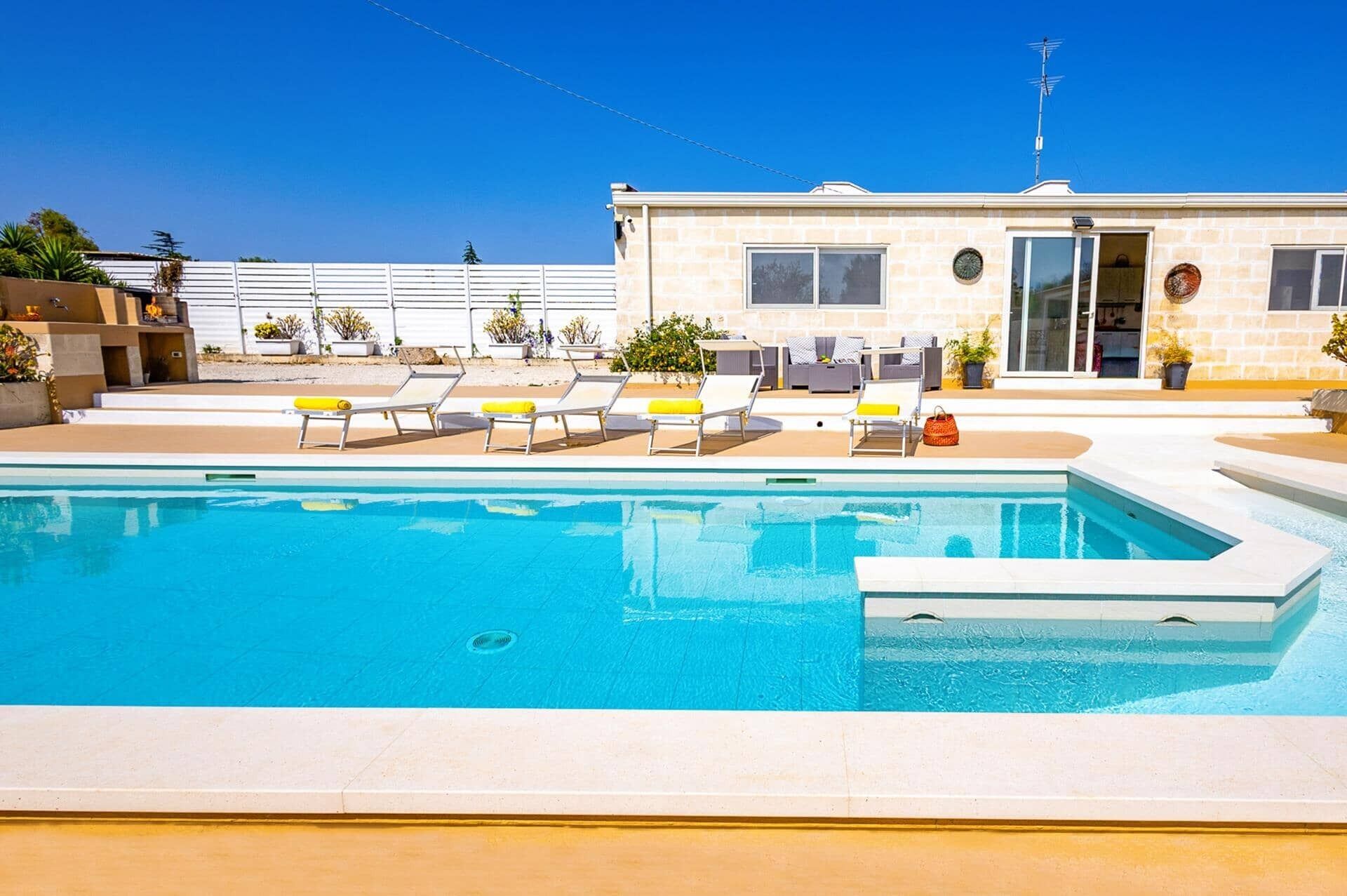 Una piscina con sillones de descanso y un edificio de fachada de piedra.
