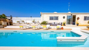 Una piscina con sillones de descanso y un edificio de fachada de piedra.