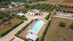 Eine Vogelperspektive auf ein Wohnanwesen mit Schwimmbad, Stein-Terrasse und umliegenden Olivenhainen.
