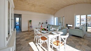 Un vaste espace de vie comprenant une table à manger pour quatre personnes, un canapé et un téléviseur fixé au mur.