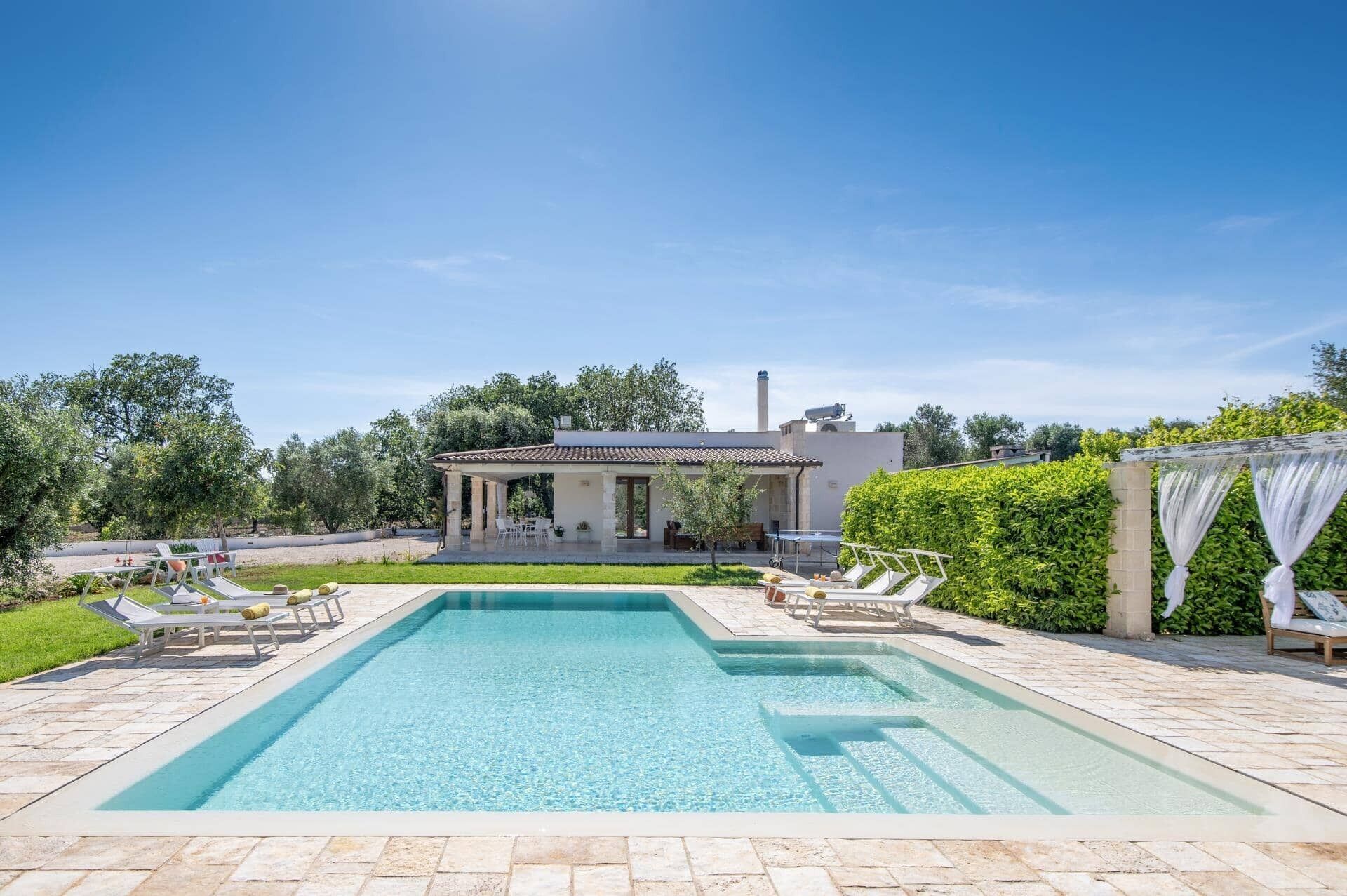 A rectangular swimming pool with lounge chairs and a covered patio area.