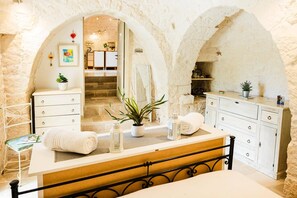 A bathroom with a stone archway, a vanity with a mirror, a sink, and a bathtub.