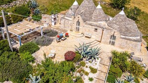 A stone building with conical roofs, outdoor seating, and a patio area. - Villa Trulli Isabella by Villa Plus (Martina Franca)