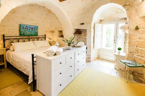 A bedroom with a stone wall, a bed with white linens, a dresser, and a painting on the wall.