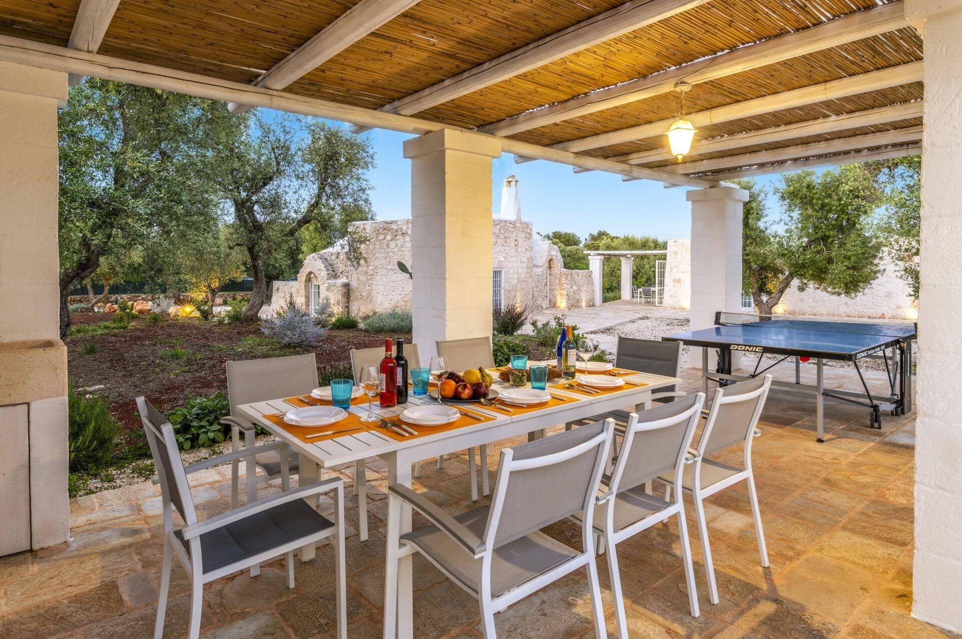 Un espace de restauration en plein air avec une table dressée pour deux personnes, une table de ping-pong et une vue sur d’anciennes ruines.