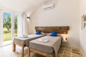 A room with two beds, a wooden headboard, an air conditioning unit, and a view of greenery outside. - Villa Trullo Acquaro by Villa Plus (Ostuni)