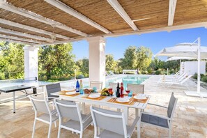 Un espacio de comedor al aire libre con vista a la piscina, sillas blancas y una mesa preparada para dos.