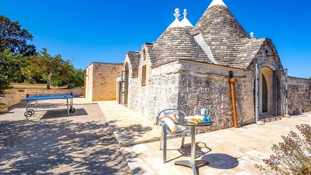 A stone building with a tiled roof and a small table with chairs in front. - Villa Trullo Bozalice by Villa Plus (Martina Franca)