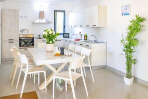 A modern kitchen with white cabinets, a stove, and a dining area with white chairs.