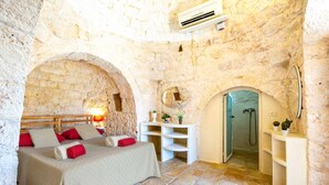 A stone-walled bedroom with a bed, a bedside table, a mirror, and a shower area.