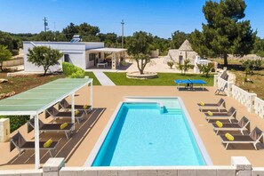 A swimming pool with lounge chairs, a ping pong table, and a stone building in the background.