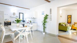 A modern kitchen with white cabinetry, a dining area with a white table and chairs, and a living room with a green sofa and yellow armchair.