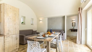 Uma sala de jantar com mesa de madeira posta para o café da manhã, um sofá e piso de ladrilho de pedra.