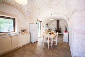 A kitchen with a window, a refrigerator, a dining table with chairs, and a clock on the wall.
