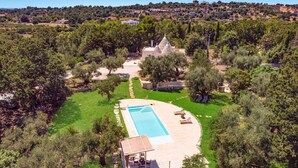 En stor privat pool med fliseterrasse, omgivet af frodig vegetation og en bygning i sten.