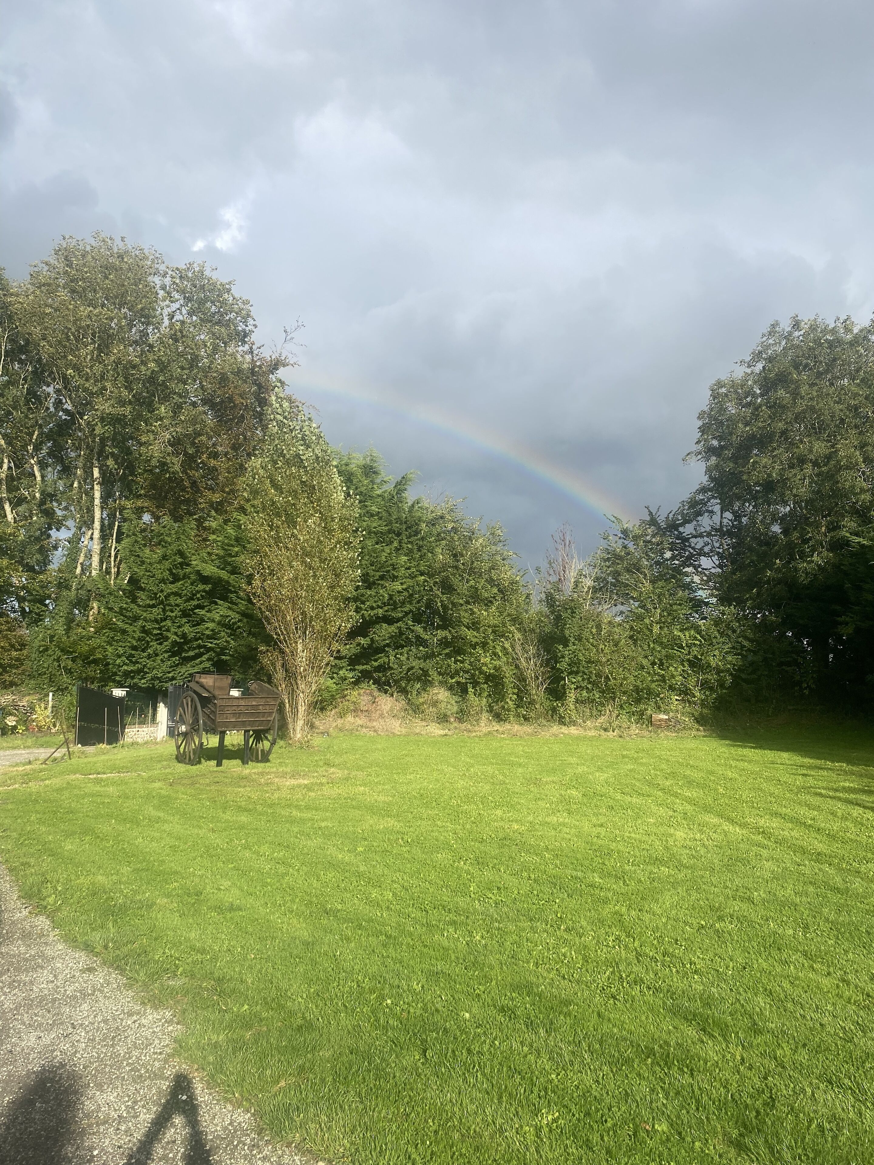 A grassy field with a wooden structure, trees, and a rainbow in the background.